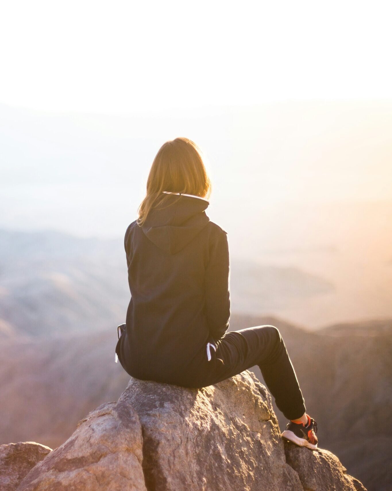 Woman sitting on a mountaintop, looking out at the view