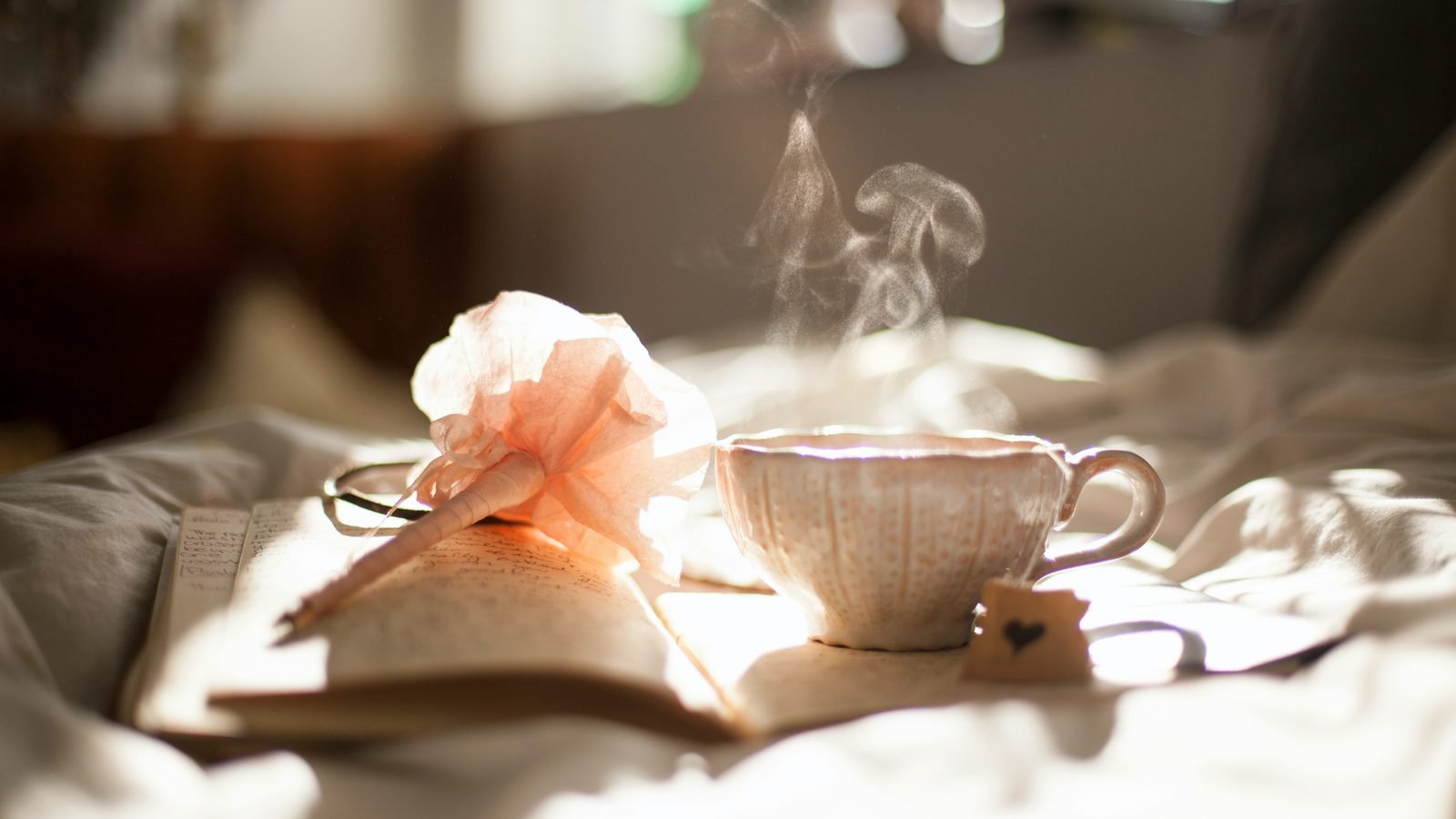 A cup of tea and an open book resting on soft bed linen in morning light