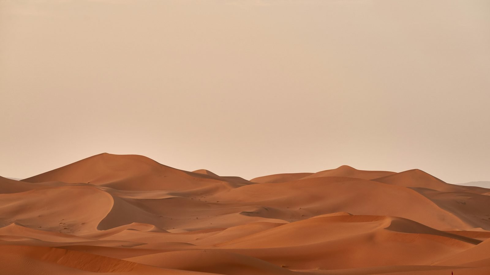 Wind lifting sand from the crest of a desert dune under a pale sky